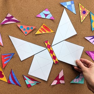 May include: A butterfly-shaped puzzle with white wings and a colorful body. Scattered around are various colorful triangle puzzle pieces with different patterns and designs. The puzzle is on a brown surface.