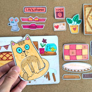May include: A collection of colorful, hand-drawn paper cutouts, including a cat, mouse, and various house-themed elements. The cat has blue eyes and is the central focus. Other items include a door, bed, and a fishbowl.