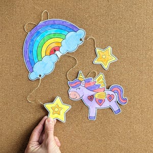 May include: A handmade mobile with a rainbow, clouds, stars, and a unicorn. The rainbow has stripes of red, orange, yellow, green, blue, and purple. The unicorn is purple with a pink mane and tail. The stars are yellow.