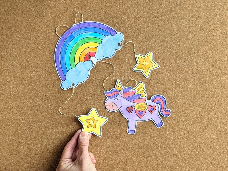 May include: A handmade mobile with a rainbow, clouds, stars, and a unicorn. The rainbow has stripes of red, orange, yellow, green, blue, and purple. The unicorn is purple with a pink mane and tail. The stars are yellow.