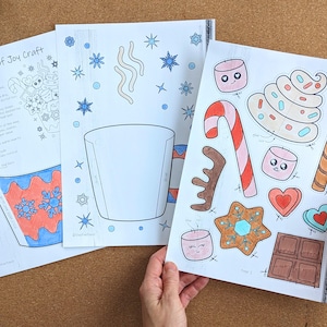 Peut inclure: Trois feuilles de papier avec un projet d'artisanat sur le th&egrave;me de l'hiver. La premi&egrave;re feuille contient des instructions et un code QR. La deuxi&egrave;me feuille a un contour de tasse et des flocons de neige. La troisi&egrave;me feuille a des images d&eacute;coup&eacute;es de bonbons, de guimauves et de biscuits en pain d'&eacute;pices.