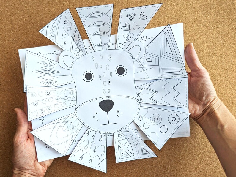 May include: A black and white lion art project with a detailed face and patterned mane. The mane is made of triangular pieces with various designs, including hearts, circles, and geometric shapes. The project is held against a corkboard background.