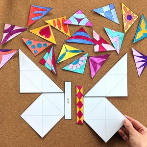 May include: A butterfly-shaped craft kit with colorful, geometric triangle pieces. The kit includes white paper shapes and smaller triangles with various designs, including hearts and flowers. The word "GLUE" is printed on one of the pieces.