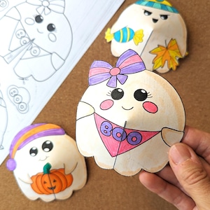 May include: Hand-colored paper ghost cutouts with cute faces and accessories. One ghost has a pink bandana with "BOO" on it. Other ghosts have hats, bows, and hold a pumpkin and candy. A sheet of ghost outlines is also visible.