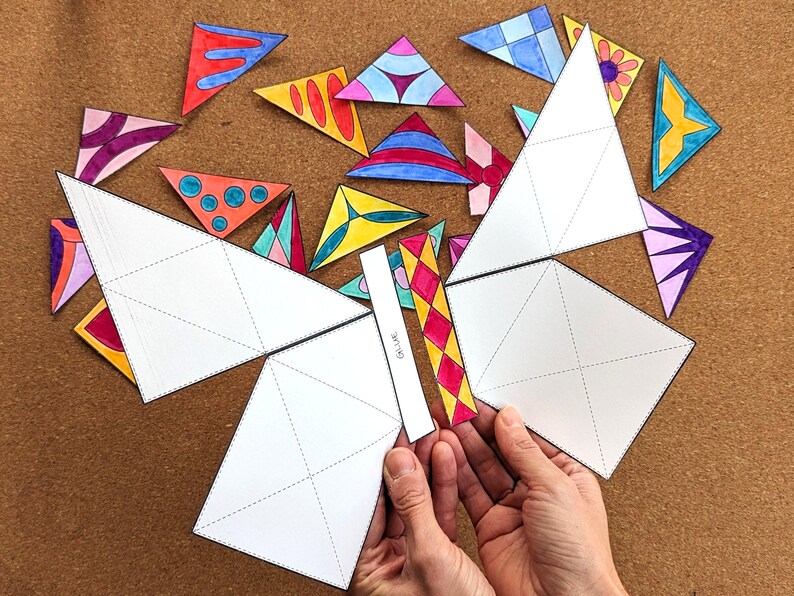 May include: A craft project featuring a butterfly design made from white paper and colorful triangle cutouts. The butterfly's wings are assembled from large white paper pieces with dotted lines. The triangles are decorated with various patterns and colors.