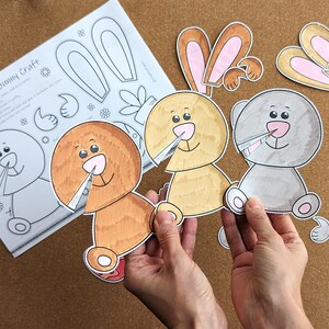 May include: A craft project featuring three bunny cutouts in shades of brown, yellow, and gray, held by hands. The cutouts have pink noses and are smiling. A sheet of paper with a bunny outline and the text "Spring Bunny Craft" is also visible.