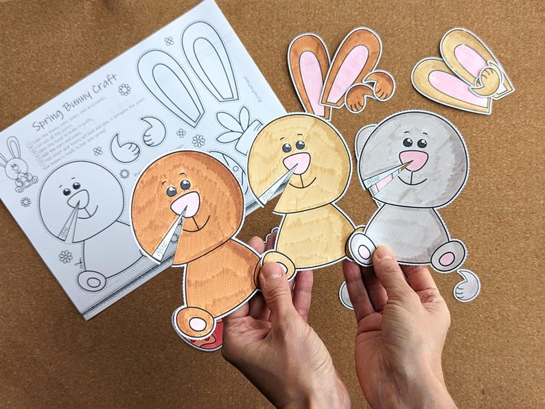 May include: A craft project featuring three bunny cutouts in shades of brown, yellow, and gray, held by hands. The cutouts have pink noses and are smiling. A sheet of paper with a bunny outline and the text "Spring Bunny Craft" is also visible.