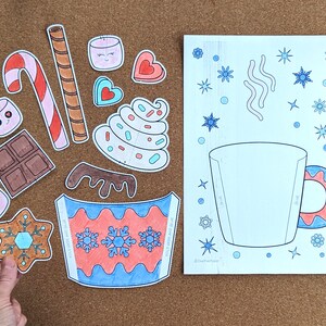 Peut inclure: Un ensemble de d&eacute;coupes en papier et une page &agrave; colorier sur le th&egrave;me de l'hiver. Les d&eacute;coupes comprennent une canne en bonbon, des guimauves, du chocolat et une tasse avec des flocons de neige. La page &agrave; colorier montre une tasse avec des flocons de neige et de la vapeur.