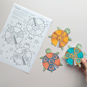 Op de afbeelding: Een knutselproject met een vel met omtrekken van schildpadden en instructies, samen met drie voltooide schildpaduitsparingen. De schildpadden zijn gekleurd in oranje, geel en blauwgroen, met groene koppen en vinnen. De tekst op het vel luidt "Bubbly Turtles craft".