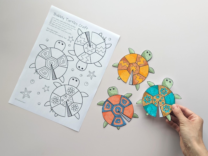Op de afbeelding: Een knutselproject met een vel met omtrekken van schildpadden en instructies, samen met drie voltooide schildpaduitsparingen. De schildpadden zijn gekleurd in oranje, geel en blauwgroen, met groene koppen en vinnen. De tekst op het vel luidt "Bubbly Turtles craft".