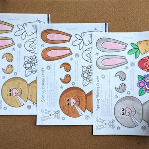 May include: Three sheets of paper with a spring bunny craft design. Each sheet features bunny ears, faces, and other spring-themed elements. The text "Spring Bunny Craft" is printed on each sheet. The sheets are on a brown surface.