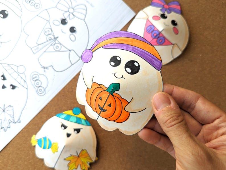 May include: Hand-drawn Halloween-themed cutouts of cartoon ghosts. One ghost holds an orange pumpkin, wearing a purple and orange hat. Other ghosts wear hats and bows. A sketch of similar ghosts is in the background.