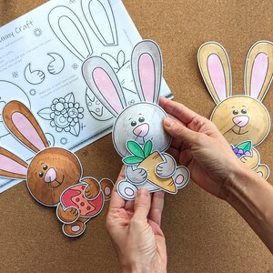 May include: A craft project featuring spring bunny cutouts. The bunnies are colored in shades of brown, gray, and tan, with pink inner ears. One bunny holds a carrot. A sheet of paper with instructions is also visible.