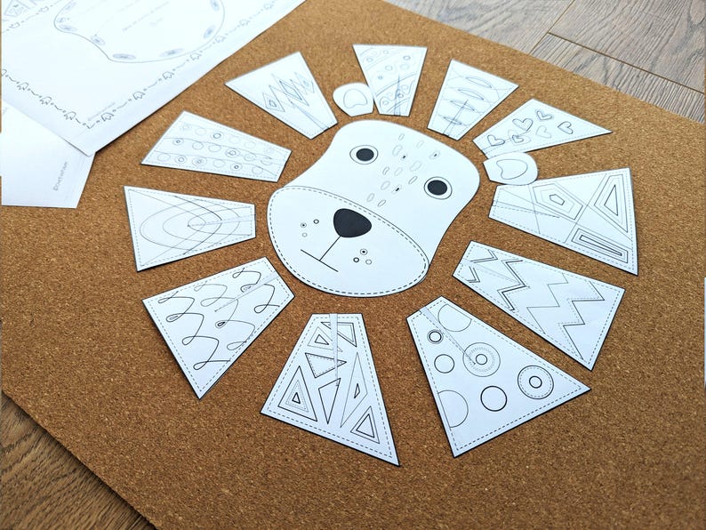 May include: A white lion face with black details and a paper mane made of various geometric shapes, arranged on a brown corkboard. The mane pieces have different patterns. A sheet of paper with a decorative border is in the upper left.