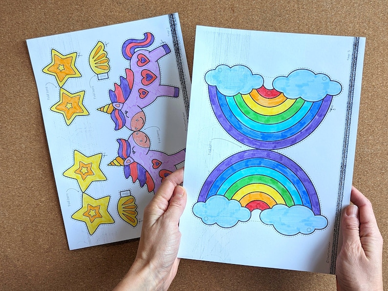 May include: Two sheets of paper with colourful illustrations. One sheet features a rainbow with blue clouds, and the other has unicorns, stars, and wings. The drawings are outlined in black and coloured with markers.