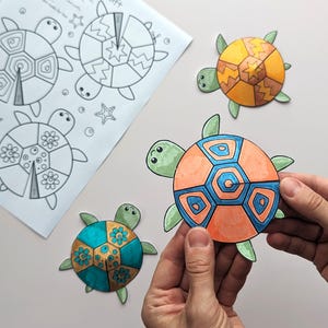 Op de afbeelding: Een kleurplaat met schildpadcontouren en drie afgewerkte, kleurrijke schildpaduitsparingen. De uitsparingen zijn oranje, blauw, groen en geel. Een uitsparing wordt door een persoon vastgehouden.