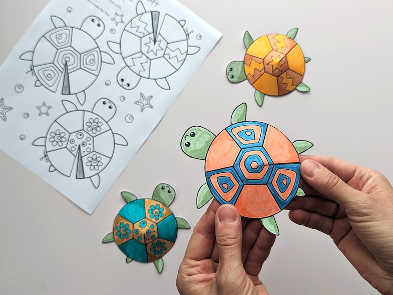 Op de afbeelding: Een kleurplaat met schildpadcontouren en drie afgewerkte, kleurrijke schildpaduitsparingen. De uitsparingen zijn oranje, blauw, groen en geel. Een uitsparing wordt door een persoon vastgehouden.