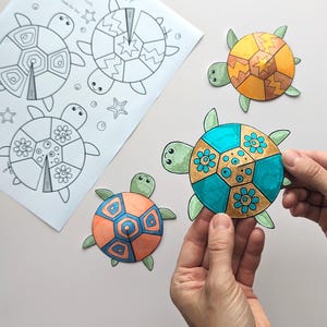 Op de afbeelding: Een vel papier met drie lijntekeningen van schildpadden en zeesterren, naast drie kleurrijke, uitgesneden schildpadvormen. Een schildpad wordt door een persoon vastgehouden. De schildpadden zijn oranje, geel en blauwgroen met groene accenten.