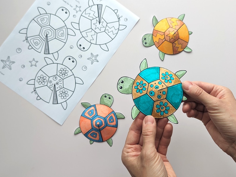 Op de afbeelding: Een vel papier met drie lijntekeningen van schildpadden en zeesterren, naast drie kleurrijke, uitgesneden schildpadvormen. Een schildpad wordt door een persoon vastgehouden. De schildpadden zijn oranje, geel en blauwgroen met groene accenten.