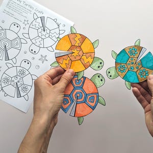 Op de afbeelding: Een knutselproject met kleurrijke schildpadontwerpen. De afbeelding toont drie voltooide schildpadden met oranje, blauwe en turquoise schilden, vastgehouden door handen. Een afgedrukte sjabloon met schildpadcontouren en de tekst "DIY Turtles Craft" is ook zichtbaar.