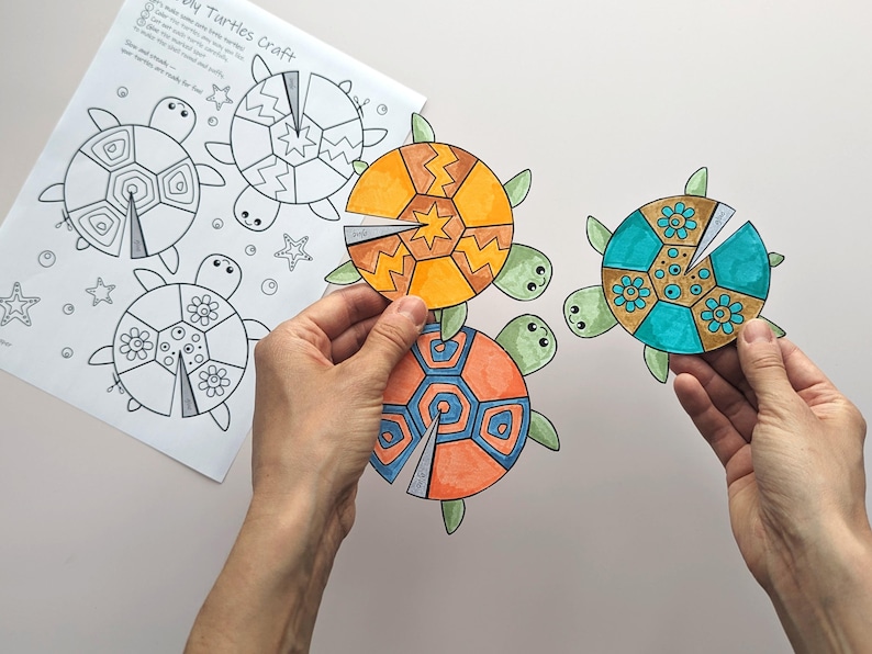 Op de afbeelding: Een knutselproject met kleurrijke schildpadontwerpen. De afbeelding toont drie voltooide schildpadden met oranje, blauwe en turquoise schilden, vastgehouden door handen. Een afgedrukte sjabloon met schildpadcontouren en de tekst "DIY Turtles Craft" is ook zichtbaar.
