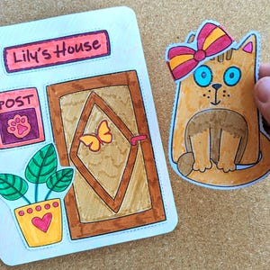 May include: Hand-drawn illustration of a cat with a bow and a house with a door, a post box, and a potted plant. The house sign reads "Lily's House". The cat is orange with blue eyes. The bow is red and yellow.