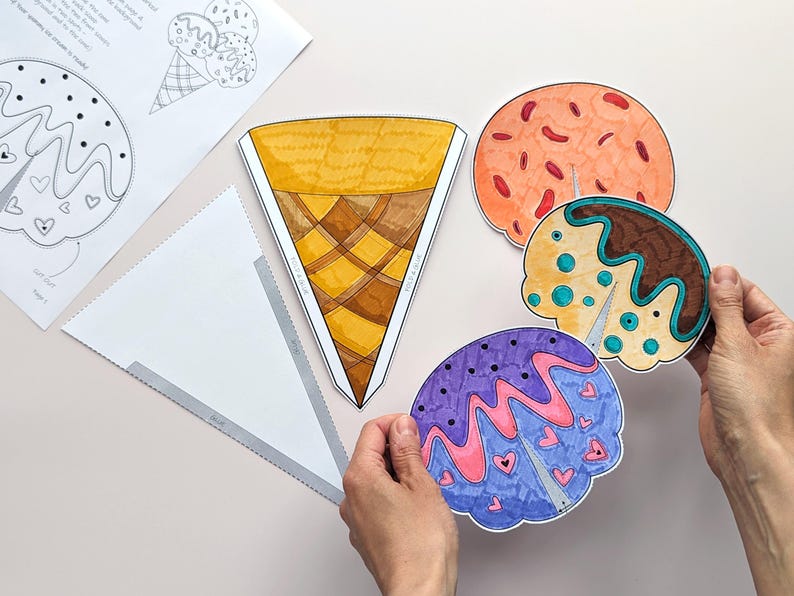 Op de afbeelding: Een verzameling kleurrijke, handgetekende ijsjes en bolletjes. De hoorn is geel en bruin, terwijl de bollen oranje, bruin en paars zijn met decoratieve details. Er zijn ook gedrukte sjablonen met ijsontwerpen.