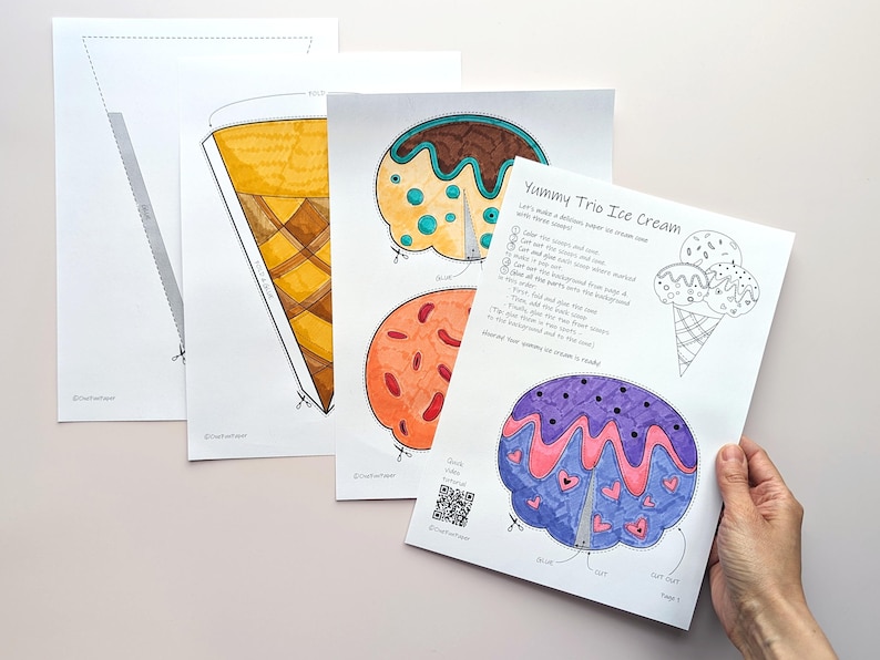 Op de afbeelding: Een verzameling afdrukbare sjablonen voor ijshoorntjes en ijsbollen. De sjablonen zijn met de hand getekend en gekleurd met aquarelverf. E&eacute;n vel heeft de tekst "Yummy Trio Ice Cream" met instructies en een QR-code.
