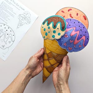 Op de afbeelding: Een handgemaakte papieren ijshoorntje met drie bollen in bruin, oranje en paars. Het hoorntje wordt door handen vastgehouden. Een zwart-wit tekening van het ijs is zichtbaar op de achtergrond. De tekst "My Trio Ice Cream" is zichtbaar.