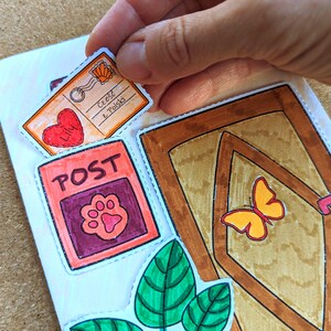 May include: Hand-drawn stickers with a postal theme. The stickers include a postcard with text, a red heart, a post office box with a paw print, a door with a butterfly, and green leaves. The stickers are being placed on a white surface.