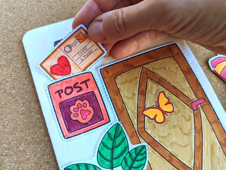 May include: Hand-drawn stickers with a postal theme. The stickers include a postcard with text, a red heart, a post office box with a paw print, a door with a butterfly, and green leaves. The stickers are being placed on a white surface.