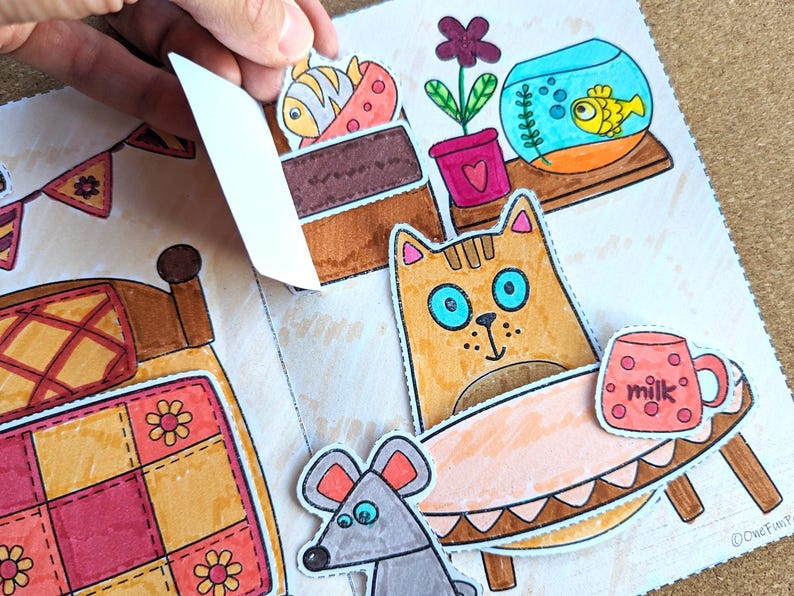 May include: A colorful, illustrated pop-up book with a cat, mouse, and fish. The cat has blue eyes and is near a table with a mug that says "milk." A fishbowl and a bed are also visible.