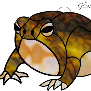 Könnte beinhalten: Eine Glasmalerei-Frosch mit einem gelben, braunen und weißen Farbschema. Der Frosch ist im Cartoon-Stil mit großen Augen und einem breiten Maul dargestellt.