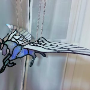 May include: A stained glass winged unicorn mobile with iridescent glass and black metal accents. The unicorn is suspended from a silver chain.