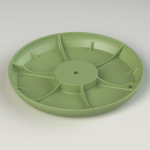 May include: A pale green, circular serving platter with a central raised section and divided compartments. The platter features radial dividers, forming pie-shaped segments. Two small holes are visible on the rim. The platter is made of a solid, durable material.