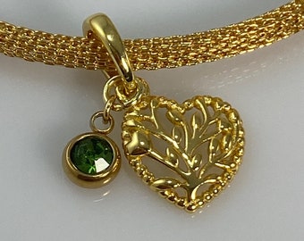 May include: Gold charm bracelet with a heart-shaped pendant featuring a tree design and a small green gemstone.