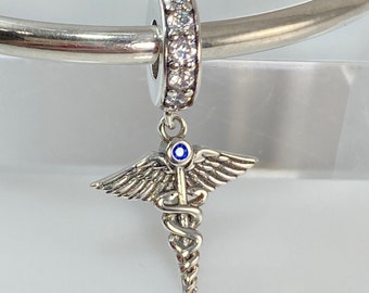 May include: Silver charm with a blue stone and a medical symbol with wings. The charm is attached to a silver bracelet.