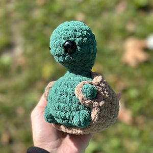 Op de afbeelding: Een gehaakt groen knuffeldier in de vorm van een schildpad met bruine gehaakte details op de schildpad. Het speelgoed heeft grote zwarte ogen en een vriendelijke uitdrukking.