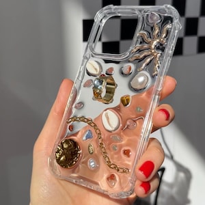 May include: A clear phone case with a variety of small objects embedded inside, including a ring, seashells, and a gold star. The objects are visible through the clear plastic.