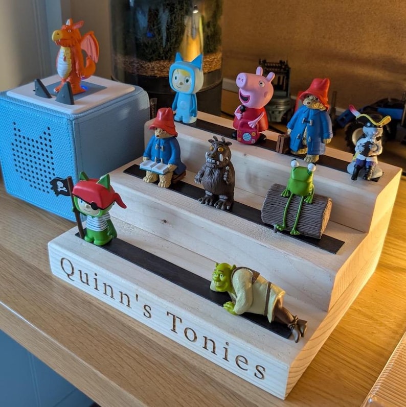 Pu&ograve; includere: Una mensola in legno a pi&ugrave; livelli, con varie statuette di personaggi. Le statuette includono un drago, un pirata, un orso, un maiale e una rana. La mensola &egrave; etichettata "Quinn's Tonies".