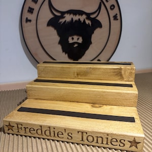 Pu&ograve; includere: Un espositore in legno a tre livelli con strisce nere e la scritta "Freddie's Tonies" e una stella. Dietro, un cartello rotondo in legno con un disegno di toro e la scritta "The Rolling Cow".