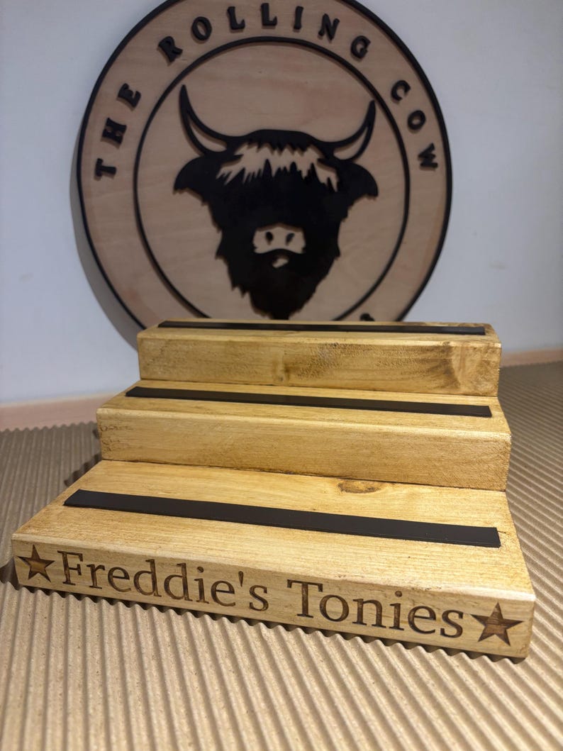 Pu&ograve; includere: Un espositore in legno a tre livelli con strisce nere e la scritta "Freddie's Tonies" e una stella. Dietro, un cartello rotondo in legno con un disegno di toro e la scritta "The Rolling Cow".