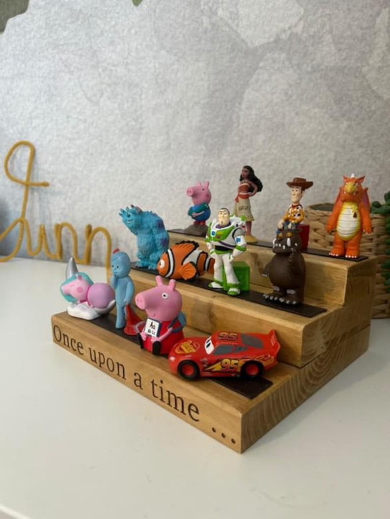 Pu&ograve; includere: Scaffale in legno a tre livelli con statuette di personaggi dei cartoni animati. Lo scaffale presenta la scritta "Once upon a time". I personaggi includono Buzz Lightyear, Woody e Saetta McQueen.