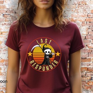 May include: A maroon t-shirt with a retro-style graphic of a cartoon Grim Reaper holding a coffee cup. The graphic is surrounded by a circle with the text "Last Responder" in white.