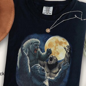 May include: Black t-shirt with a graphic print of three gray apes in front of a full moon. The text "Comfort Colors" and "XL - TG - EG" is printed on the tag.