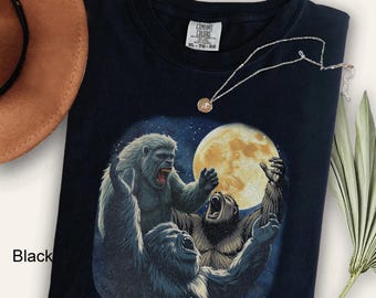 May include: Black t-shirt with a graphic print of three gray apes in front of a full moon. The text "Comfort Colors" and "XL - TG - EG" is printed on the tag.