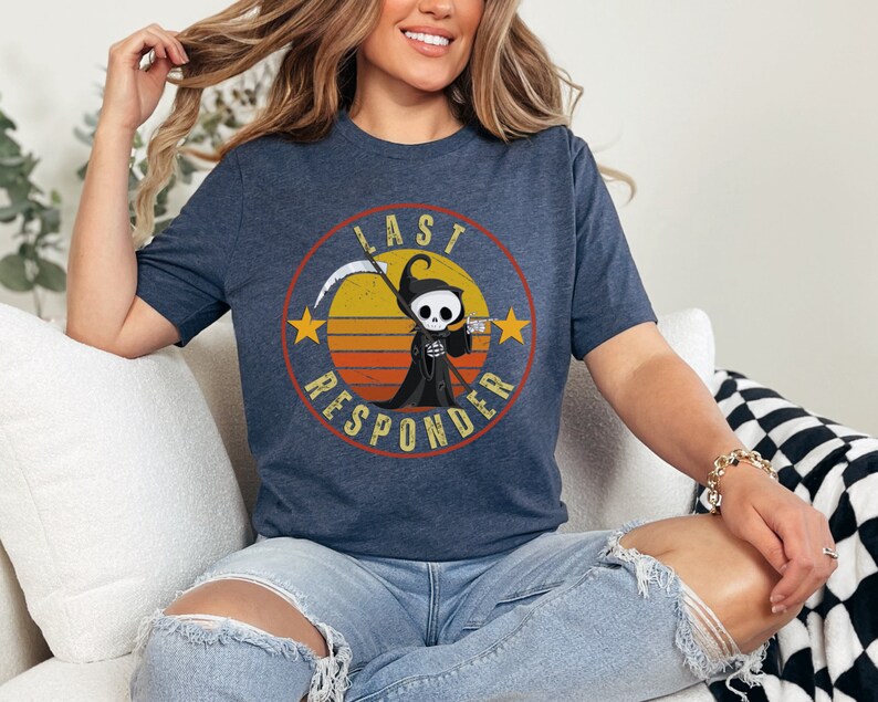 May include: A navy blue t-shirt with a retro-style graphic of a cartoon Grim Reaper holding a drink. The graphic is surrounded by a circle with the text "Last Responder" in a vintage font.