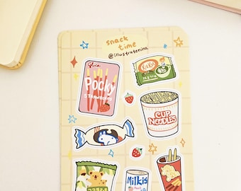 May include: A sheet of stickers featuring various Japanese snacks, including Pocky, Kit Kat, Cup Noodles, and Koala March. The stickers are on a yellow background with white stars.