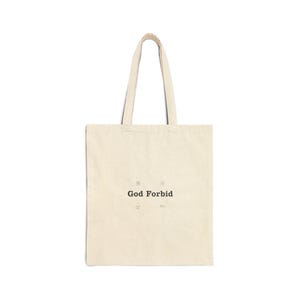 May include: Cream-colored tote bag with black text that reads "God Forbid." The bag has two handles and a simple design. The bag is made of a canvas-like material and is suitable for carrying various items.