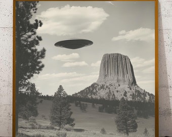 May include: A black and white photograph of a flying saucer hovering over a large rock formation in a landscape with trees. The rock formation is called Devils Tower National Monument.
